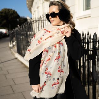 Blonde lady standing outside white buildings in chelsea, wearing an all back outfit, taupe jumper and a hand printed festive flamingos design scarf with black sunglasses on