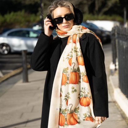 Blonde lady standing outside white buildings in chelsea, wearing an all back outfit, taupe jumper and a hand printed pumpkins design scarf with black sunglasses on