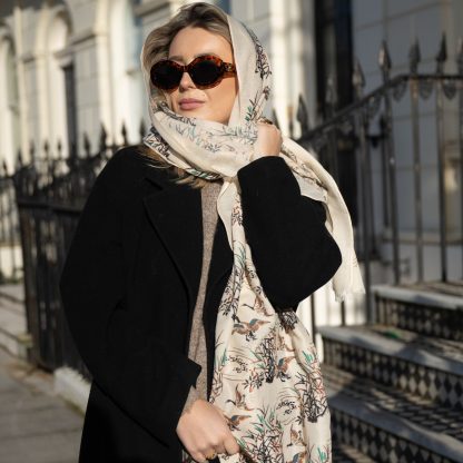 Blonde lady standing outside white buildings in chelsea, wearing an all back outfit, taupe jumper and a hand printed wild ducks design scarf with black sunglasses on