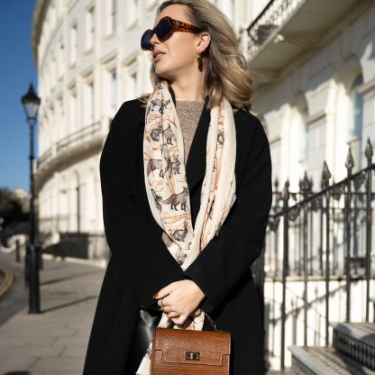 Blonde lady standing outside white buildings in chelsea, wearing an all back outfit, taupe jumper and a hand printed woodland animals design scarf with black sunglasses on