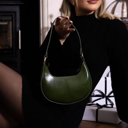 blonde lady sitting in front of fire place with christmas presents holding a olive green genuine italian leather bag