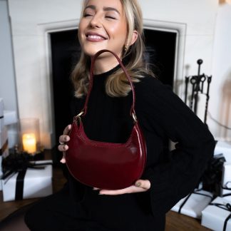 blonde lady sitting in front of fire place with christmas presents holding a burgundy plum red genuine italian leather bag