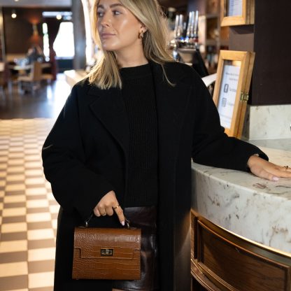 Blonde lady holding tan genuine italian leather croc crossbody bag, standing at a bar in chelsea in black outfit , holding a glass of champagne