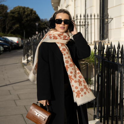 Blonde lady standing outside white buildings in chelsea, wearing an all back outfit, taupe jumper and a hand printed gingerbread man design scarf with black sunglasses on holing a tan italian leather crossbody bag