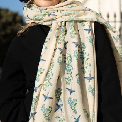 Blonde lady standing outside white buildings in chelsea, wearing an all back outfit, taupe jumper and a hand printed blue birds design scarf with black sunglasses on