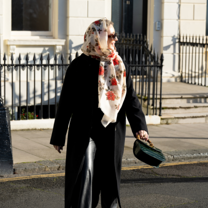 Blonde lady standing outside white buildings in chelsea, wearing an all back outfit, taupe jumper and a hand printed poinsettia design scarf with black sunglasses on