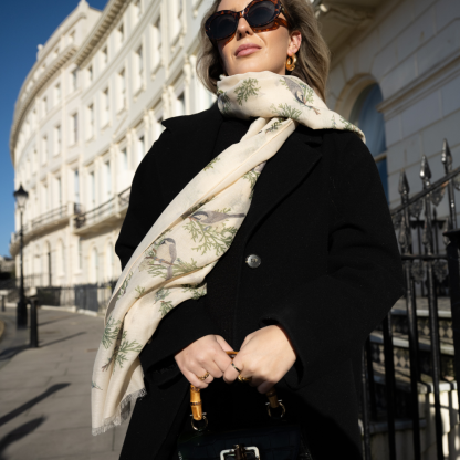 Blonde lady standing outside white buildings in chelsea, wearing an all back outfit, taupe jumper and a hand printed finch birds design scarf with black sunglasses on