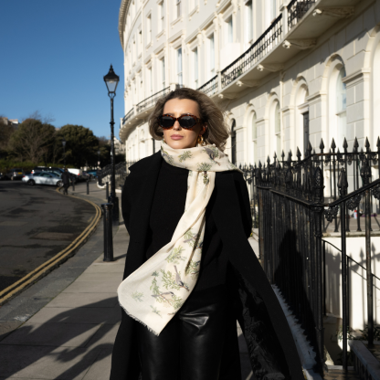 Blonde lady standing outside white buildings in chelsea, wearing an all back outfit, taupe jumper and a hand printed finch birds design scarf with black sunglasses on