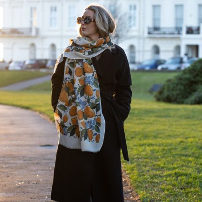 Blonde lady standing outside white buildings in chelsea, wearing an all back outfit, taupe jumper and a hand printed lemons and hydrangeas design scarf with black sunglasses on