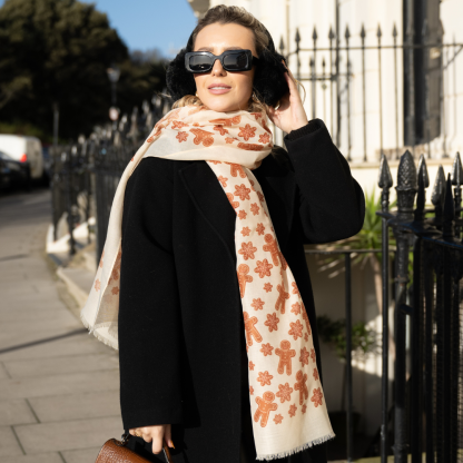 Blonde lady standing outside white buildings in chelsea, wearing an all back outfit, taupe jumper and a hand printed gingerbread man design scarf with black sunglasses on holing a tan italian leather crossbody bag