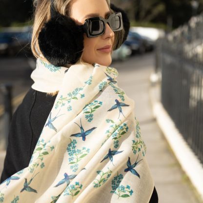 Blonde lady standing outside white buildings in chelsea, wearing an all back outfit, taupe jumper and a hand printed blue birds design scarf with black sunglasses on