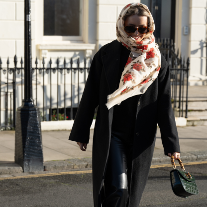 Blonde lady standing outside white buildings in chelsea, wearing an all back outfit, taupe jumper and a hand printed poinsettia design scarf with black sunglasses on