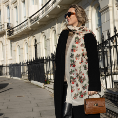 Blonde lady standing outside white buildings in chelsea, wearing an all back outfit, taupe jumper and a hand printed bows and pinecones design scarf with black sunglasses on