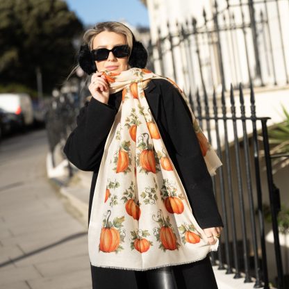 Blonde lady standing outside white buildings in chelsea, wearing an all back outfit, taupe jumper and a hand printed pumpkins design scarf with black sunglasses on