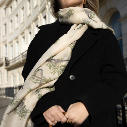 Blonde lady standing outside white buildings in chelsea, wearing an all back outfit, taupe jumper and a hand printed finch birds design scarf with black sunglasses on