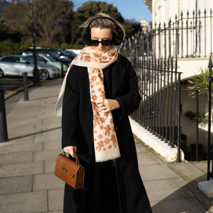 Blonde lady standing outside white buildings in chelsea, wearing an all back outfit, taupe jumper and a hand printed gingerbread man design scarf with black sunglasses on holing a tan italian leather crossbody bag