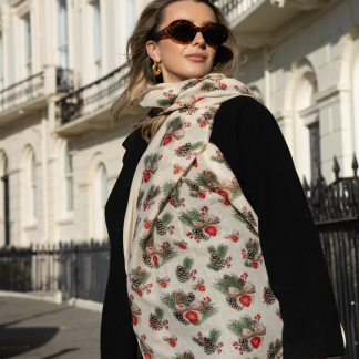 Blonde lady standing outside white buildings in chelsea, wearing an all back outfit, taupe jumper and a hand printed bows and pinecones design scarf with black sunglasses on