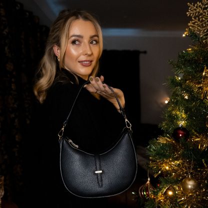 Blonde lady holding black genuine italian leather bag in front of christmas tree as a gift for her this christmas