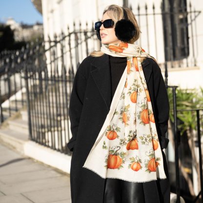 Blonde lady standing outside white buildings in chelsea, wearing an all back outfit, taupe jumper and a hand printed pumpkins design scarf with black sunglasses on