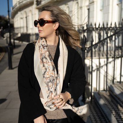 Blonde lady standing outside white buildings in chelsea, wearing an all back outfit, taupe jumper and a hand printed woodland animals design scarf with black sunglasses on