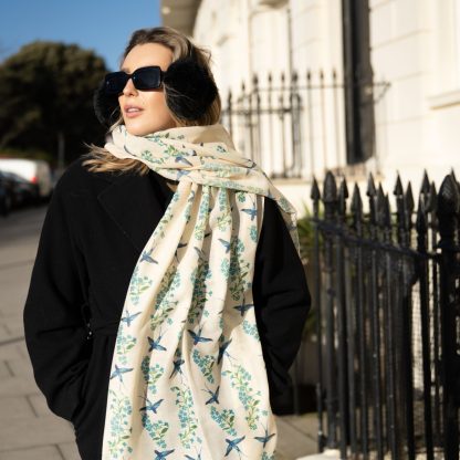 Blonde lady standing outside white buildings in chelsea, wearing an all back outfit, taupe jumper and a hand printed blue birds design scarf with black sunglasses on