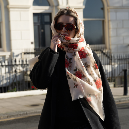 Blonde lady standing outside white buildings in chelsea, wearing an all back outfit, taupe jumper and a hand printed poinsettia design scarf with black sunglasses on