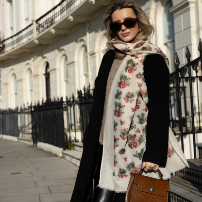 Blonde lady standing outside white buildings in chelsea, wearing an all back outfit, taupe jumper and a hand printed bows and pinecones design scarf with black sunglasses on