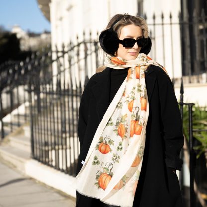 Blonde lady standing outside white buildings in chelsea, wearing an all back outfit, taupe jumper and a hand printed pumpkins design scarf with black sunglasses on