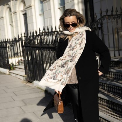 Blonde lady standing outside white buildings in chelsea, wearing an all back outfit, taupe jumper and a hand printed wild ducks design scarf with black sunglasses on