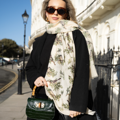 Blonde lady standing outside white buildings in chelsea, wearing an all back outfit, taupe jumper and a hand printed finch birds design scarf with black sunglasses on