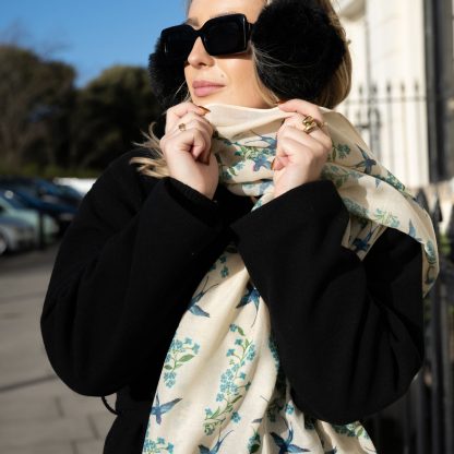 Blonde lady standing outside white buildings in chelsea, wearing an all back outfit, taupe jumper and a hand printed blue birds design scarf with black sunglasses on