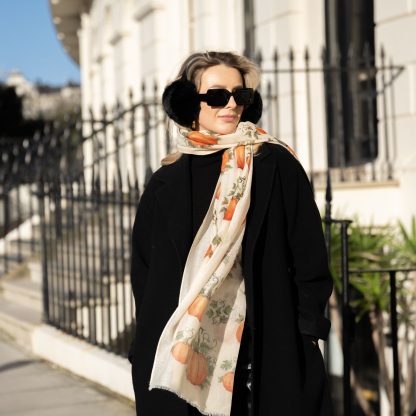 Blonde lady standing outside white buildings in chelsea, wearing an all back outfit, taupe jumper and a hand printed pumpkins design scarf with black sunglasses on