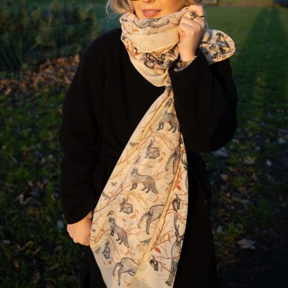 Blonde lady standing outside white buildings in chelsea, wearing an all back outfit, taupe jumper and a hand printed woodland animals design scarf with black sunglasses on