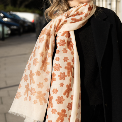 Blonde lady standing outside white buildings in chelsea, wearing an all back outfit, taupe jumper and a hand printed gingerbread man design scarf with black sunglasses on holing a tan italian leather crossbody bag