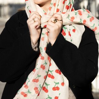 Blonde lady standing outside white buildings in chelsea, wearing an all back outfit, taupe jumper and a hand printed cherries design scarf with black sunglasses on