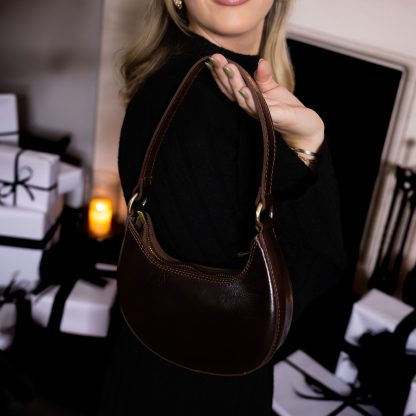 blonde lady sitting in front of fire place with christmas presents holding a Dark brown chocolate genuine italian leather bag