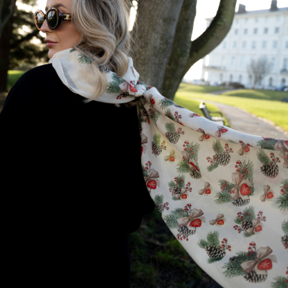 Blonde lady standing outside white buildings in chelsea, wearing an all back outfit, taupe jumper and a hand printed bows and pinecones design scarf with black sunglasses on