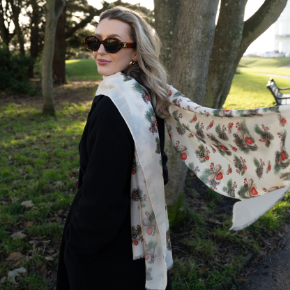 Blonde lady standing outside white buildings in chelsea, wearing an all back outfit, taupe jumper and a hand printed bows and pinecones design scarf with black sunglasses on